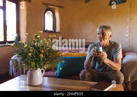Thoughtful caucasian mature man looking away while having coffee at home. simple living, lifestyle, drink and refreshment. Stock Photo