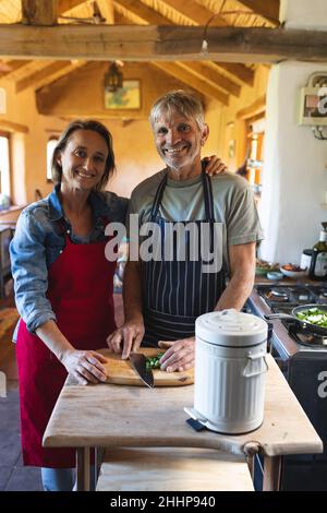 Portrait of smiling caucasian mature couple cooking food together in kitchen at home. simple living, togetherness, lifestyle and cooking. Stock Photo
