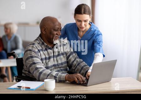 Young woman nurse helping black senior man using laptop Stock Photo