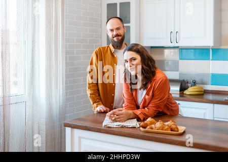 Portrait of Happy Smiling couple in kitchen. Caucasian Husband and wife 30s in kitchen at home. Hapy man and woman Looks into camera in cozy home Stock Photo
