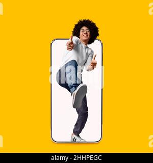 Smiling young curly attractive mixed race guy show fingers at camera on big phone blank screen Stock Photo