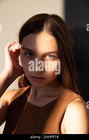 Portrait in sunset light of woman with dark hair and white skin isolated on beige with face in shadow Stock Photo
