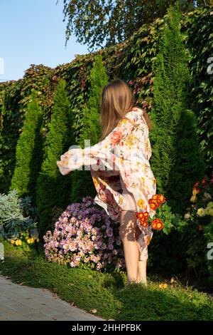 Standing young woman with white skin with greenery behind in floral dress Stock Photo
