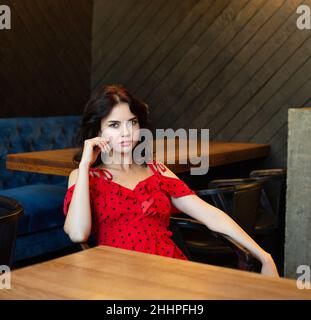 Sitting young dark haired woman with white skin in dark wooden room with luxury chandelier Stock Photo