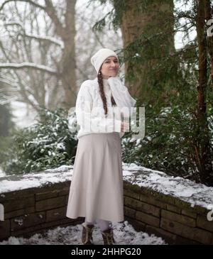 Smiling dressed warm young european woman with pigtails in park with snow Stock Photo