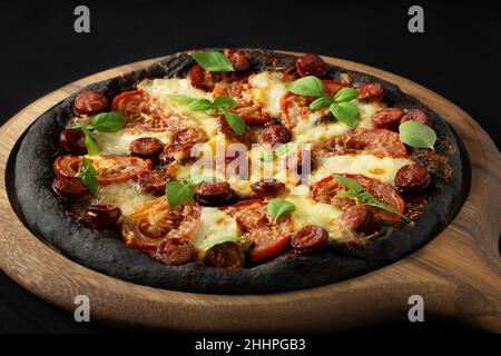 Black pizza with tomatoes, sausages, mozzarella and basil. Dough with healthy bamboo charcoal powder. Stock Photo