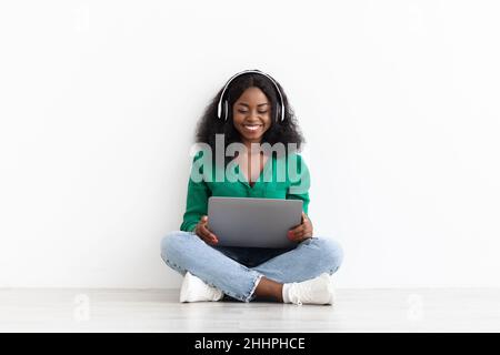Positive young black lady using laptop and headset Stock Photo