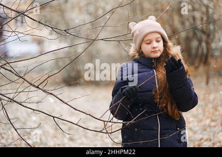 Cute little girl holding a tree branch without leaves on a background of falling snowflakes. First snow concept. Stock Photo