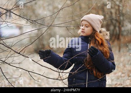 Cute little girl holding a tree branch without leaves on a background of falling snowflakes. First snow concept. Stock Photo