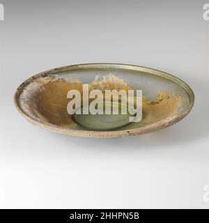 Glass dish 4th century A.D. Roman Translucent green.Tubular, slightly outsplayed rim, folded out, down, and in, forming a prominent flanged edge to side; convex curving side sloping in to applied solid foot ring with diagonal tooling marks around its outer side; slightly convex bottom.Around the flanged edge to rim, a single horizontal groove. Broken and repaired, with only one small hole; some bubbles, elongated in rim; thick, limy encrustation, dulling, and slight iridescence.Greenish, colored blown glass.. Glass dish  249340 Stock Photo