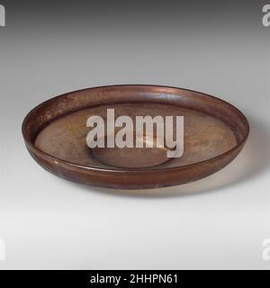 Glass dish 4th–5th century A.D. Roman Translucent purple.Tubular rim, folded out and down, forming flange covering side, with an inward fold at base; low convex curving side and broad floor to body, sloping gently downwards to tubular, inward-sloping foot ring, made by folding; flat bottom.One large hole in bottom, but complete otherwise; some pinprick bubbles; dulling and iridescent weathering.Violet, plain blown glass.. Glass dish  249341 Stock Photo