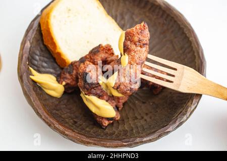 Romanian grilled minced meat rolls, mici or mititei on a carved  wooden bowl with mustard and a wooden traditional fork, isolated on white background Stock Photo