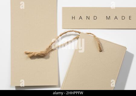 Three cardboard rectangular brand tags of gray-brown color with inscription on top right label saying item is hand made and rope on bottom right one Stock Photo