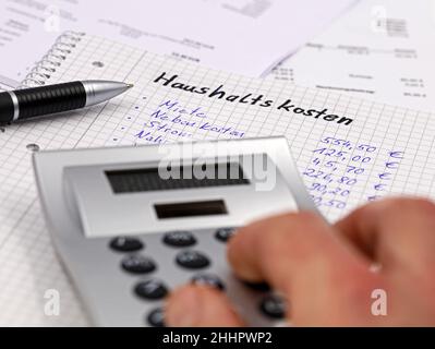 Calculating monthly household expenses with a calculator in german Stock Photo