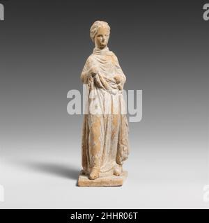 Terracotta statuette of a draped woman early 3rd century B.C. Greek, Attic The figure is holding up her garment with both hands at waist level, and she appears to be wearing shoes.. Terracotta statuette of a draped woman  247499 Stock Photo