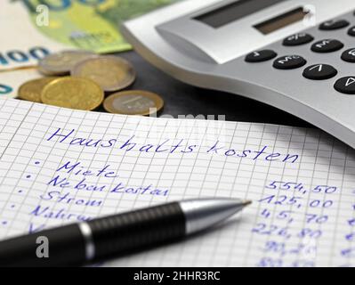 list of the expenses of a private household in german language on notepad with pen, coins and calculator, close up Stock Photo