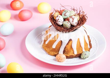 Easter cake with colorful eggs in a chocolate nest on pink background. Happy Easter concept. Dessert also known as  Kuglof. Stock Photo