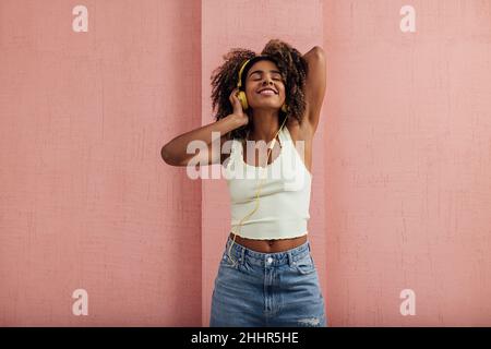 Happy woman standing at wall listening to music with her eyes closed Stock Photo