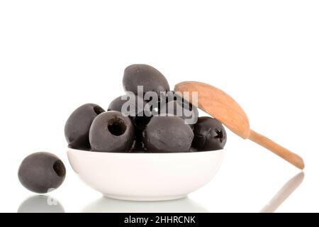 A few pickled black olives in a white saucer with a wooden spoon, macro, isolated on white. Stock Photo