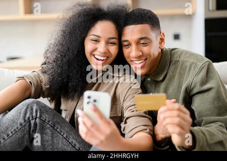 Overjoyed biracial couple shopping together online. Excited multiracial woman and man holding smartphone and a credit card. Purchases online, making order, buying something in e-shop Stock Photo