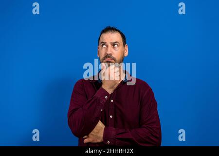 Thinking man isolated on blue background. Closeup portrait of a casual young pensive businessman looking up at copy space. Caucasian male model Stock Photo
