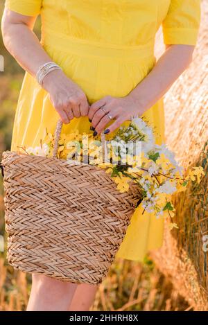 a girl in a yellow dress holds a basket of yellow flowers Stock Photo