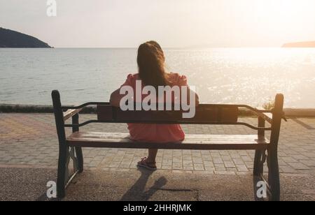 Young woman relaxing on a bench near the sea during sunset Stock Photo