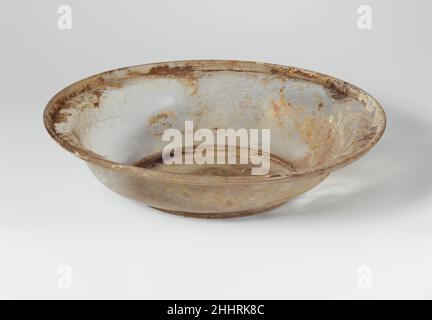 Glass dish 4th century A.D. Roman Colorless with faint yellow green tinge.Tubular, flaring rim, folded out and down, with almost horizontal inner shoulder; S-shaped side to body, curving in to integral tubular base ring; slightly concave bottom, thicknened at center with small pontil scar.Broken and repaired, cracked on one side and a large hole in the other; pinprick bubbles; pitting, iridescent weathering, and some limy encrustation around rim.. Glass dish  239890 Stock Photo