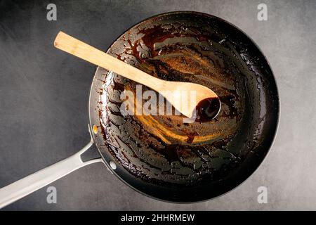 Dirty Nonstick Skillet and Wooden Spoon Used to Make a Balsamic Reduction: An unwashed frying pan and bamboo spoon covered in a sticky glaze Stock Photo