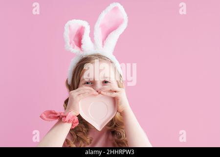 happy modern girl in pink dress with heart shape saucer and bunny ears isolated on pink background. Stock Photo