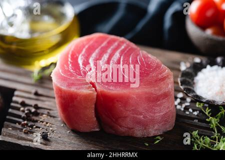 Raw pink tuna steak and spices on wooden cutting board, closeup view Stock Photo
