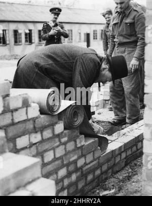 Prime Minister Winston Churchill in action as bricklayer.During a visit to an anti-aircraft battery the Prime Minister saw some soldiers bricklaying. He asked them if the 'had their tickets' as bricklayers and then said 'Here let me lay one for you.' Picture shows the Prime Minister expertly laying bricks, watched by the soldiers. 6th April, 1942 Stock Photo