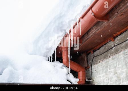 A snowdrift on the roof of a house from which icicles hang. Cleaning roofs from accumulated snow. Stock Photo