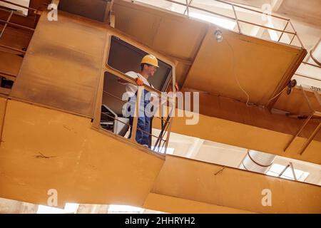 Cheerful builder standing in operator cabin of overhead crane Stock Photo