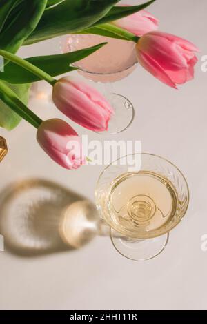 pink tulips in brass vase and white wine drink cocktail in coupe glass on white backdrop Stock Photo