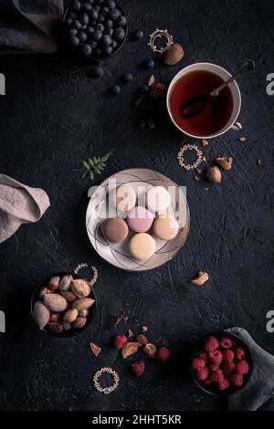 macaroons in a plate. the macaroon a small French almond cake. top view with blueberries, almonds, raspberry end a cup of tea. copy space for text Stock Photo