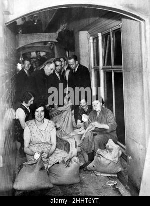 Making sandbags in the shelter - Women are making and men filling sandbags in the basement of the India building in the city. The basement of this building is  to be an official shelter. 28th September 1938. Stock Photo