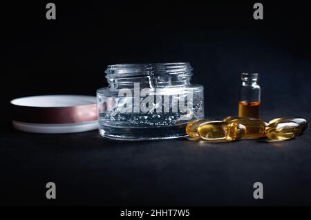 transparent jar with moisturizing cream with hyaluronic acid and vitamins in capsules on a black background Stock Photo