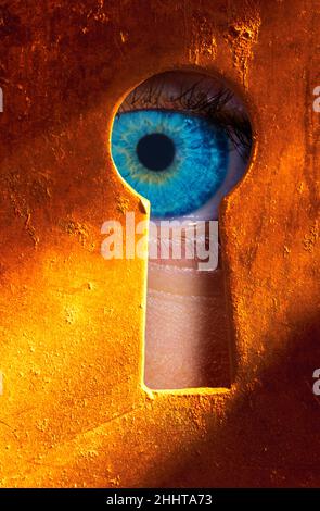 Eye peering through a keyhole Stock Photo