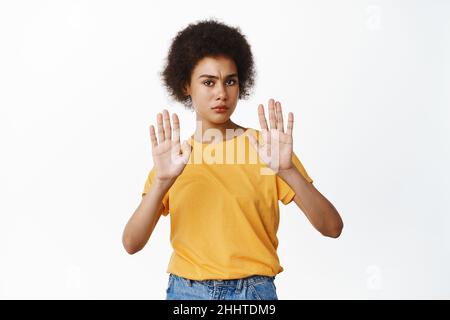 Stop. Concerned serious Black woman showing block, taboo gesture, saying no, raising palms in refusal, prohibit gesture, standing against white Stock Photo