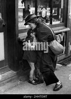 Twenty four year old warden Mrs Mary Couchman crouches down to protect her young son Brian and his two friends during an air in a Kent village during the Second World War.She was smoking a cigarette on a break between warnings in the warden's post when she saw her four year old son playing some distance away with two friends. When the sirens sounded again she ran out of the post and towards the children with bombs falling around her, instinctively protecting them from flying shrapnel and debris by huddling over them. October 1940. Stock Photo
