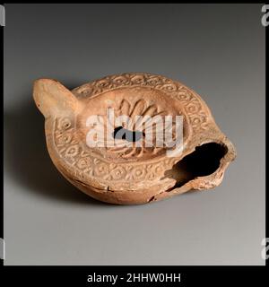 Terracotta oil lamp late 3rd century A.D. Roman, Cypriot Loeschcke Type 8. Unpierced handle. Mold-made. Discus; rosette with hollow, overlapping petals around central filling hole. Shoulder: chain pattern of circles and dots within two incised lines. On slightly concave base, inscribed in Greek letters: C?PI?/WNOC. Broken around nozzle, partially repaired but left side missing; small hole extending towards handle from filling hole.. Terracotta oil lamp. Roman, Cypriot. late 3rd century A.D.. Terracotta. Late Imperial. Terracottas Stock Photo