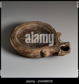 Terracotta oil lamp 1st half of 1st century A.D. Roman, Cypriot Loeschcke Type 1A, with broad, ornate nozzle channel. Mold-made. Discus: crane facing left, with reeds and ground line; below crane's neck, a single filling hole, with a broad band of lines and grooves towards edge. Volutes flanking nozzle. Within incised base ring, uneven base, with impressed letters across center: FAVSTI, and small, impressed dots above and below. Intact.. Terracotta oil lamp. Roman, Cypriot. 1st half of 1st century A.D.. Terracotta. Early Imperial. Terracottas Stock Photo
