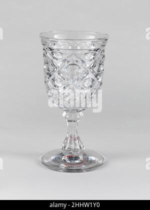Goblet 1850–60 American With the development of new formulas and techniques, glass-pressing technology had improved markedly by the late 1840s. By this time, pressed tablewares were being produced in large matching sets and innumerable forms. During the mid-1850s, colorless glass and simple geometric patterns dominated. Catering to the demand for moderately-priced dining wares, the glass industry in the United States expanded widely, and numerous factories supplied less expensive pressed glassware to the growing market. At the Exhibition of the Industry of All Nations at New York’s Crystal Pal Stock Photo
