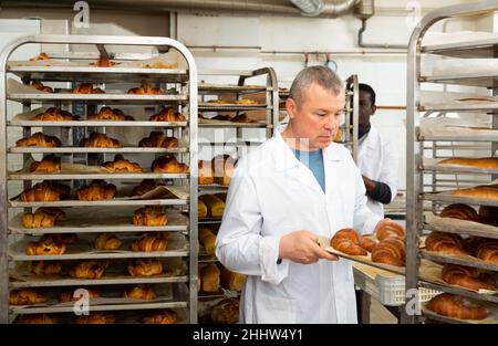 Baker arranging trays with bakery products on trolley Stock Photo