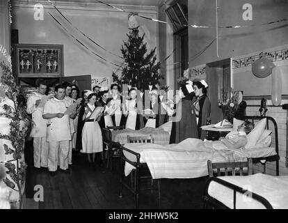 Carols in the wards at Salford Royal Hospital. Christmas Eve, Nurses and medical staff of the Salford Royal Hospital went round the hospital wards and sang carols to the patients, to cheer their Christmas Eve. Here, in a decorated ward, is one way of spending Xmas Eve, bringing a little comfort to others. Greater Manchester, December 1952. P002736 Stock Photo