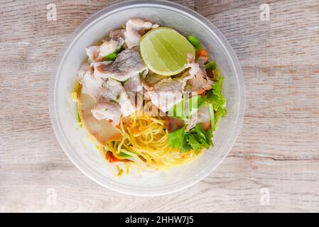 Top view Thai and China Asian food yellow noodles lemon lime, Dry noodles pork with red roasted pork and vegetable in plastic bowl on wooden table Stock Photo