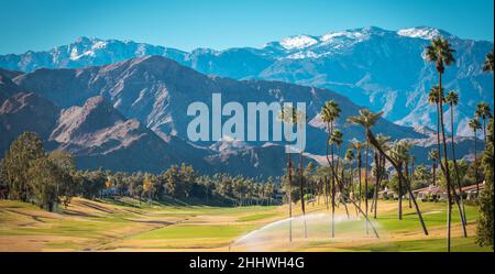 Sunny Warm Winter Time in the Palm Desert Coachella Valley. Golf Courses, Palms and Mountains Covered by Fresh Snow. Recreation in Southern California Stock Photo