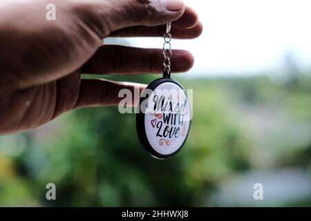 Hand of a man holding a round keychain with the inscription "Mixed with Love" on a soft blurred background Stock Photo