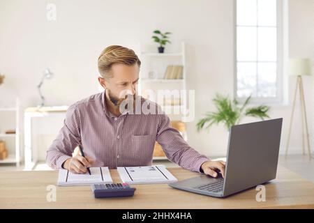 Serious businessman calculates company's internal accounts using laptop and calculator. Stock Photo